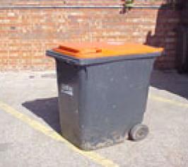 A grey trade waste bin with an orange lid
